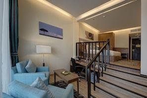 A hotel room with a sofa, a desk, a lamp, a painting, a staircase, and a bed.