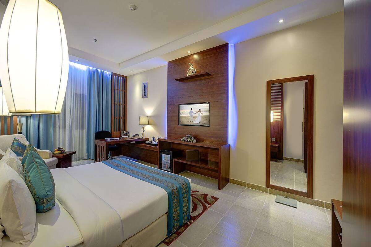 A hotel room with a large bed, a desk, a TV, and a mirror.