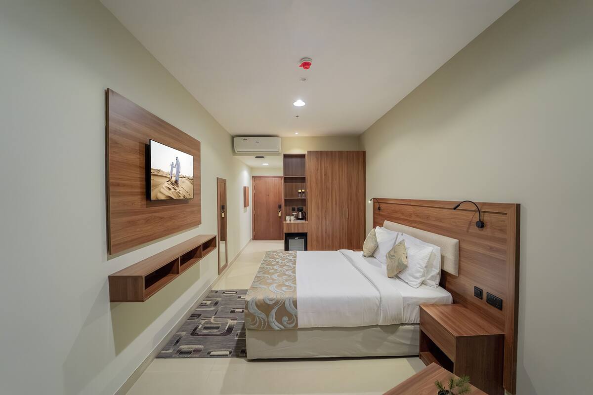 A modern bedroom with a large bed, a TV mounted on the wall, built-in wardrobes, and a small desk.