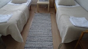 A room with two single beds, a small table with a lamp, a window with curtains, and a radiator. - Koivukankare (Kaarina)
