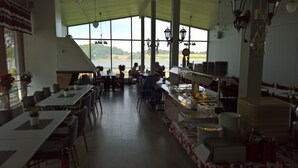 A restaurant with large windows, tables, chairs, and a counter with plates and utensils. - Koivukankare (Kaarina)