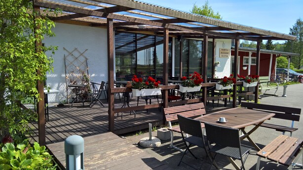 An outdoor seating area with tables and chairs, a reception desk, and a pergola with a roof. - Koivukankare (Kaarina)