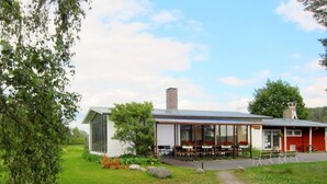 A modern building with a glass extension, outdoor seating, and a red facade. - Koivukankare (Kaarina)