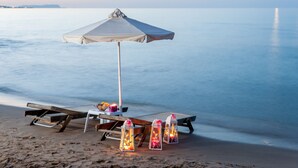 Ein Strandarrangement mit Tisch, Bank, Sonnenschirm und dekorativen Laternen.