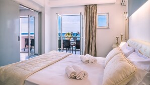Ein Hotelzimmer mit einem großen Bett, einem Balkon mit Tisch und Stühlen und Meerblick.