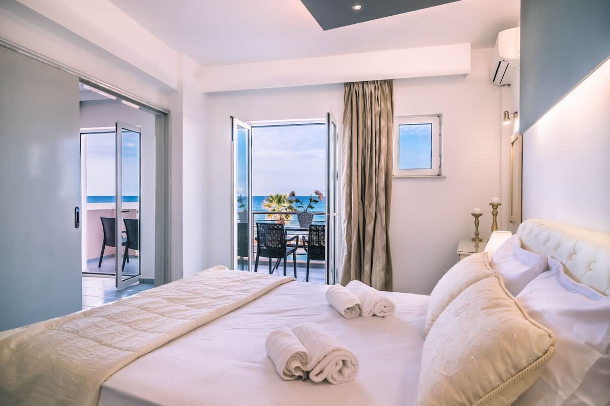 A hotel room with a large bed, a balcony with a table and chairs, and a view of the sea.