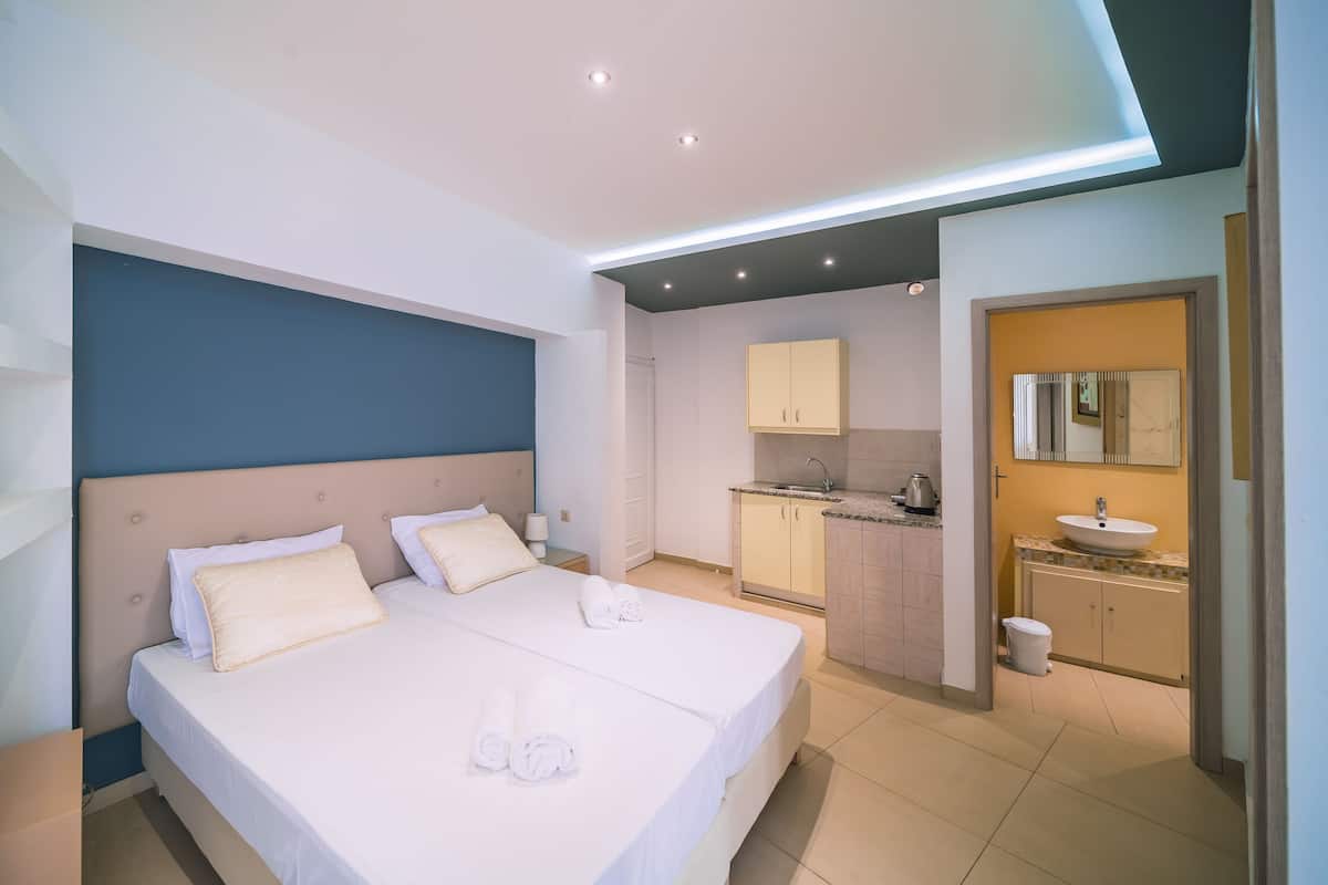A modern hotel room with a large bed, a separate bathroom, and a kitchenette.