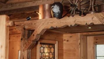 A rustic wooden interior with a wooden ceiling, a window with a lattice design, and a wooden shelf with a copper pot and a decorative item.