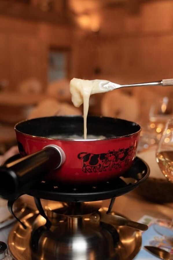 Una olla roja sobre una hornilla con una cuchara sopera sosteniendo una sustancia cremosa.