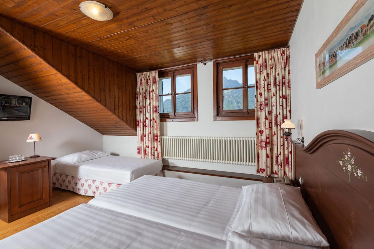 Ein Schlafzimmer mit zwei Betten, Holzboden, Heizkörper und einem Fenster mit Vorhängen.