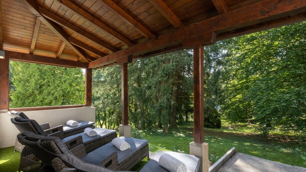 Un espacio de estar al aire libre cubierto, con mobiliario de mimbre y vistas a un jardín exuberante.