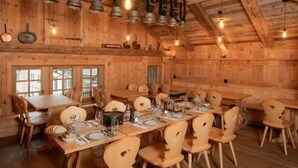 Un comedor rústico de madera con vigas a la vista, mesas y sillas de madera, y lámparas colgantes.
