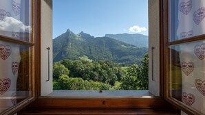 Una habitación con marco de ventana de madera y cortinas con estampado de corazones, que ofrece vistas a un paisaje montañoso.