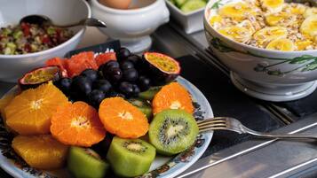 Un plato de frutas frescas, como naranjas, kiwi, maracuyá y uvas, con un tazón de cereales y una ensalada al fondo.