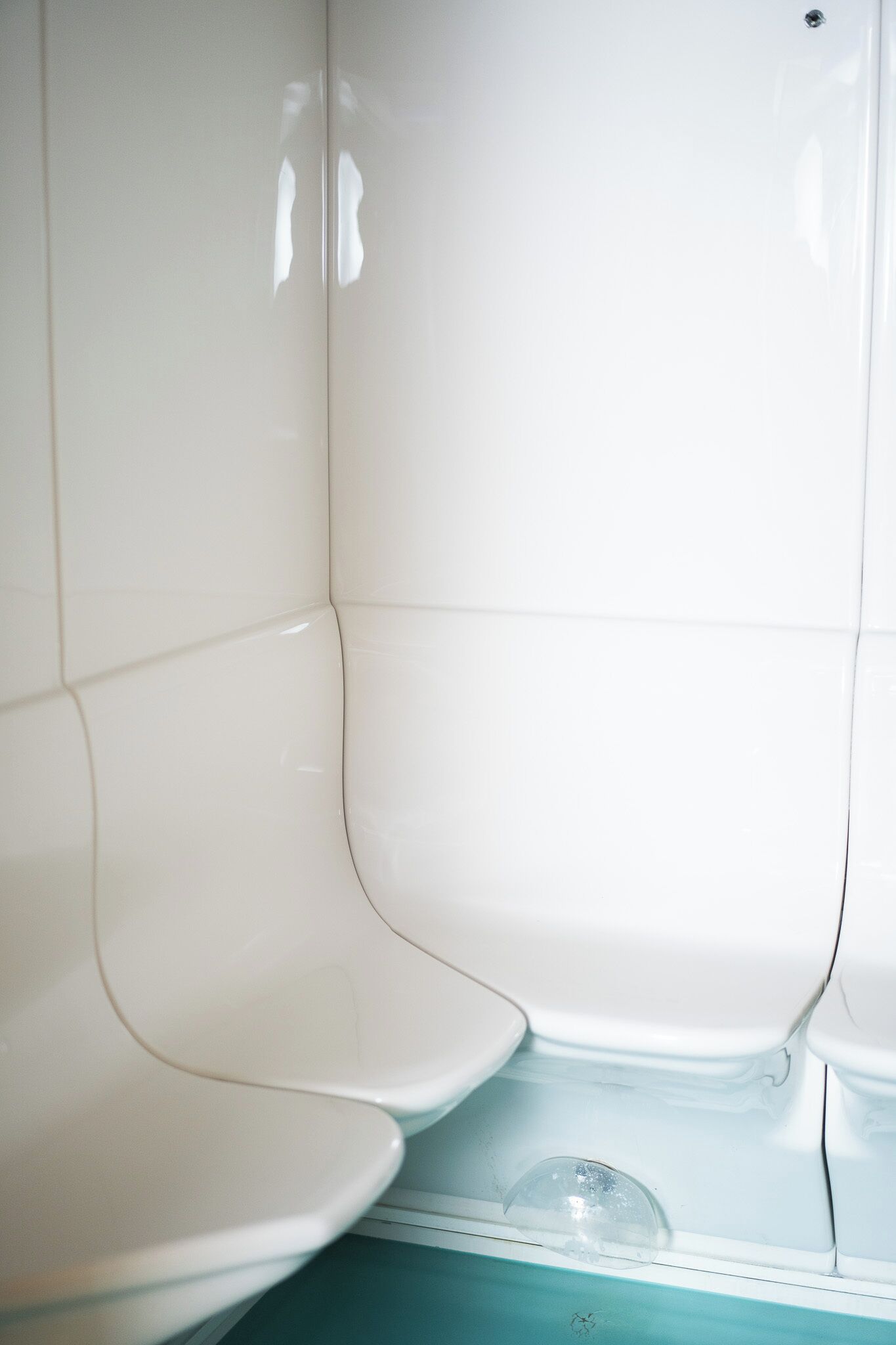 Esquina de un baño con azulejos blancos y un inodoro.