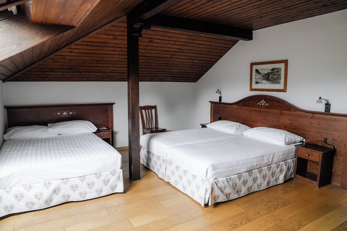 Ein Schlafzimmer mit zwei Betten, Holz-Kopfteilen, einer Holzbalkendecke, einem Nachttisch und einem gerahmten Bild an der Wand.