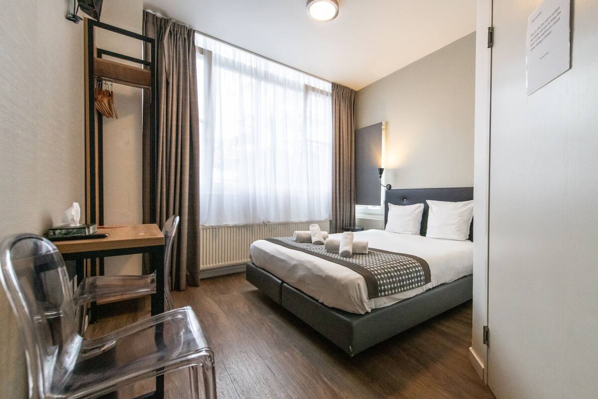 A hotel room with a bed, a desk, a chair, and a window with curtains.