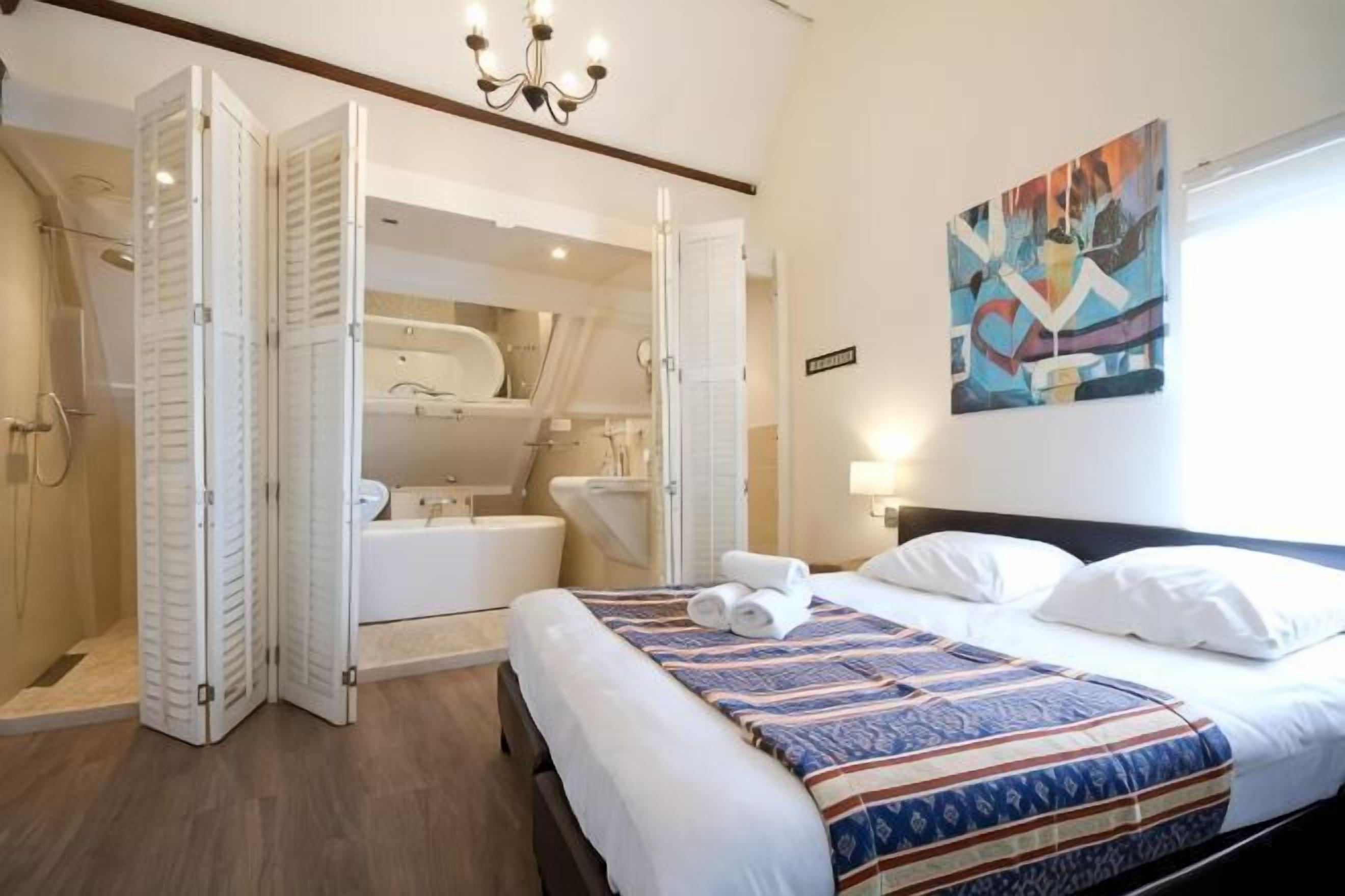 Ein Schlafzimmer mit Bett, Dusche, Badewanne und einem großen Spiegel.