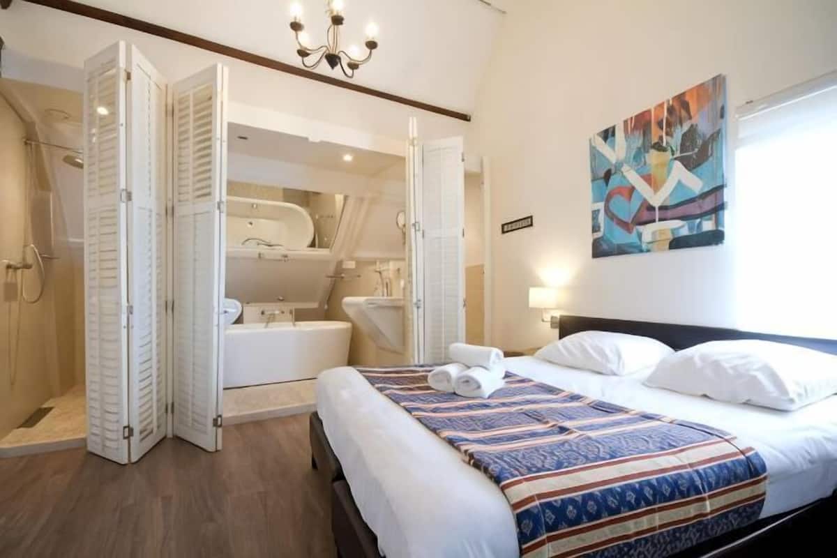 A bedroom with a bed, a shower, a bathtub, and a large mirror.