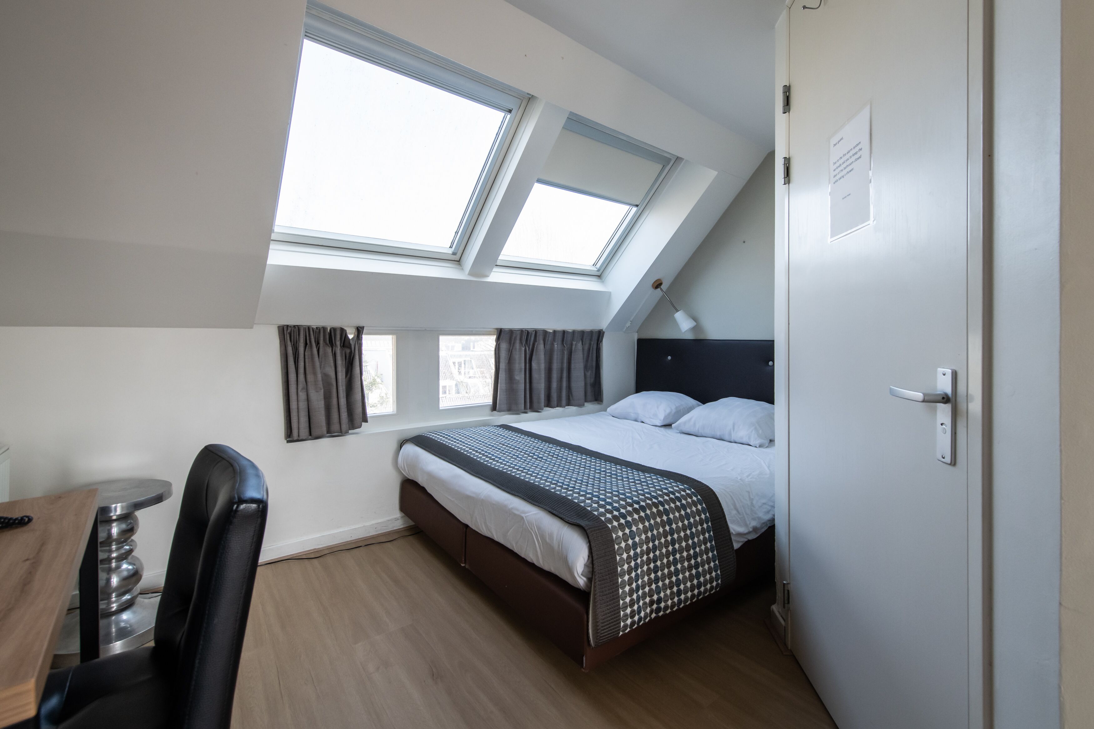 Un dormitorio con cama, escritorio y silla. Hay tragaluces sobre la cama.