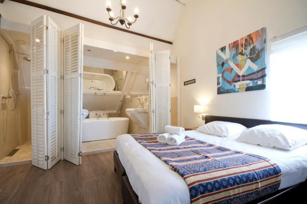 A bedroom with a bed, a shower, a bathtub, and a large mirror.