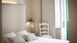 A bedroom with a bed, pillows, a chair, a nightstand, and a window with blinds. - Palazzo Bregante (Monopoli)