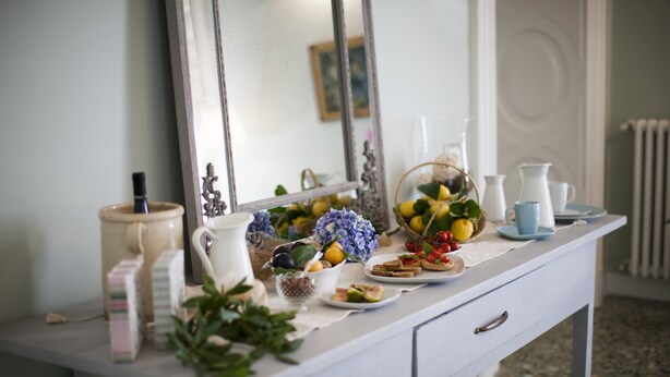 A white dresser with a mirror, a vase of flowers, and various food items. - Palazzo Bregante (Monopoli)