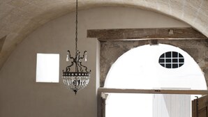 An arched doorway with a white door, a chandelier, and a small window in a room with stone walls. - Palazzo Bregante (Monopoli)