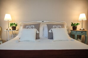A neatly made bed with white linens, two decorative pillows with floral embroidery, and two bedside tables with lamps and potted plants.