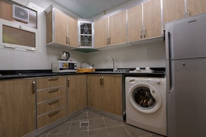 Una cocina compacta con armarios de madera, microondas integrado, lavadora y refrigerador de acero inoxidable.