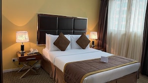 Ein Hotelzimmer mit einem großen Bett, zwei Nachttischlampen, einem Nachttisch mit Telefon und einem Fenster mit Vorhängen.