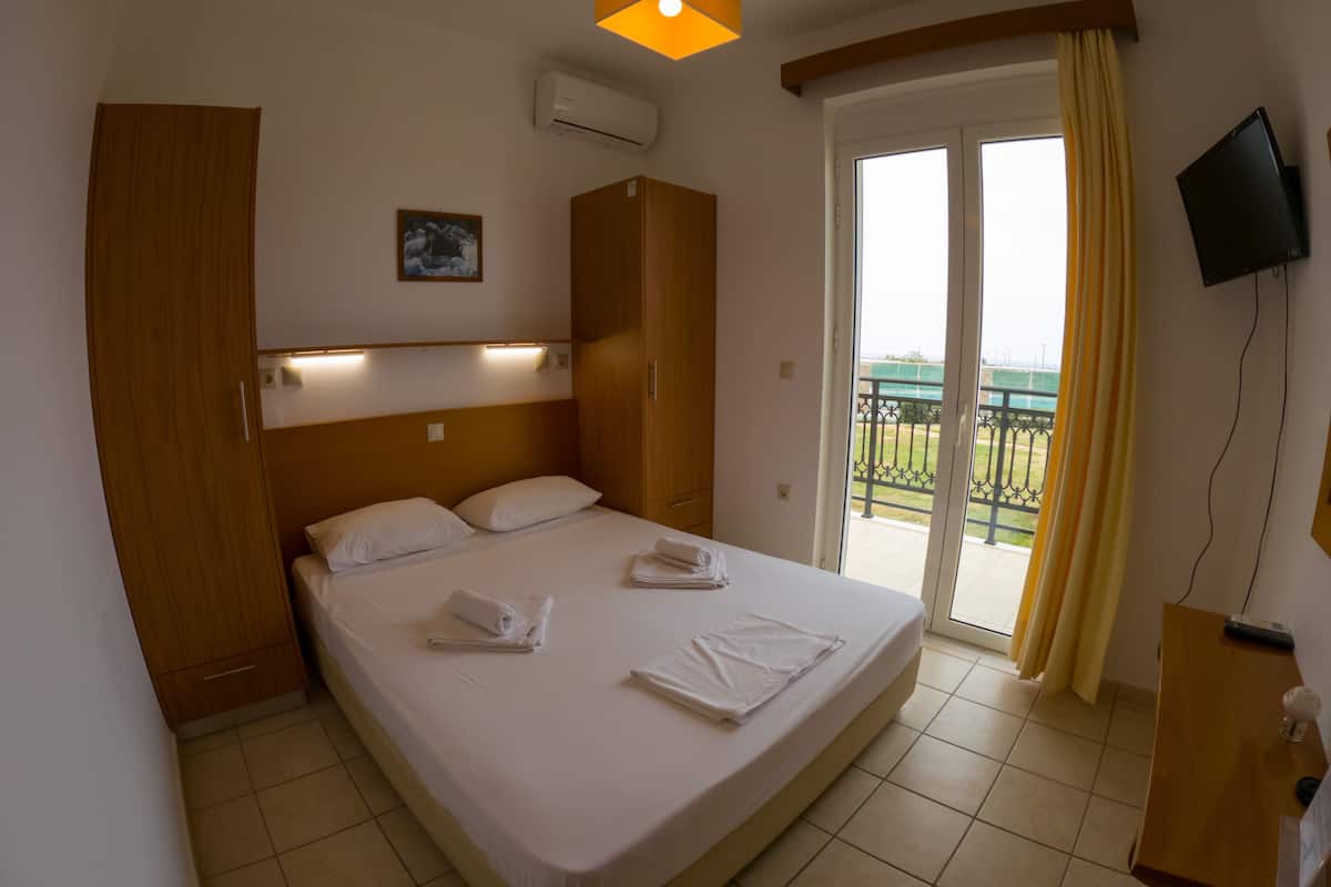 A hotel room with a bed, a TV, a balcony with a view, and a wooden wardrobe.