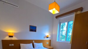 Habitación de hotel con una cama grande, dos mesitas de noche, un velador, una ventana con cortinas y dos lámparas de pared.