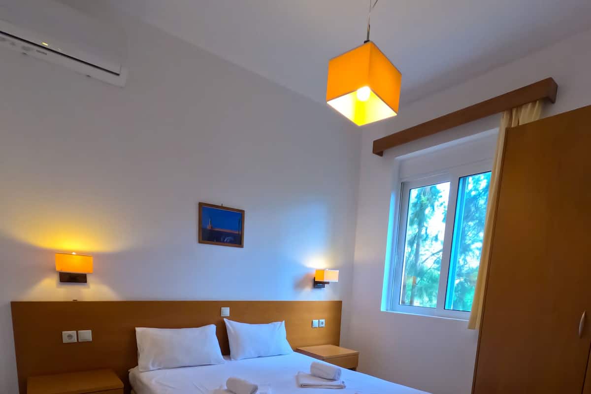 A hotel room with a large bed, two bedside tables, a nightstand, a window with curtains, and two wall-mounted lamps.