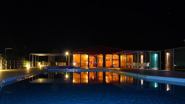 Vista nocturna de un hotel con piscina, un área exterior techada y un interior bien iluminado.