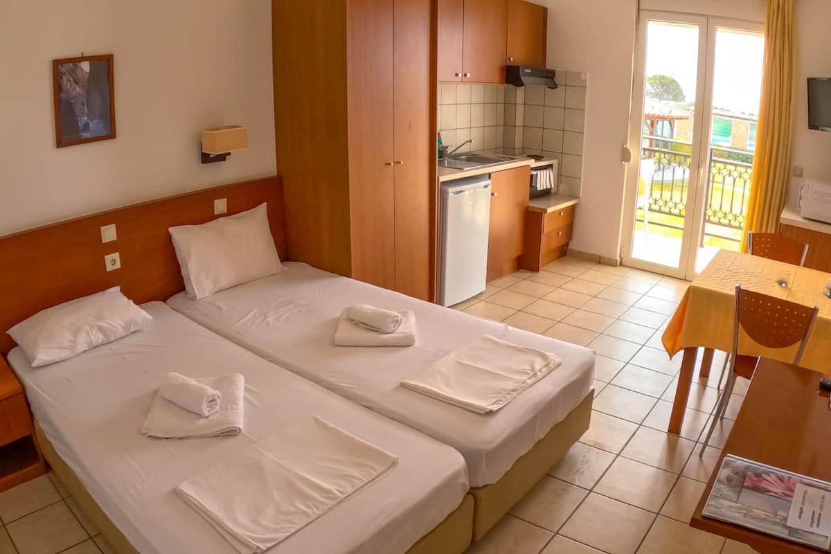 A hotel room with two beds, a kitchenette, and a balcony with a view.