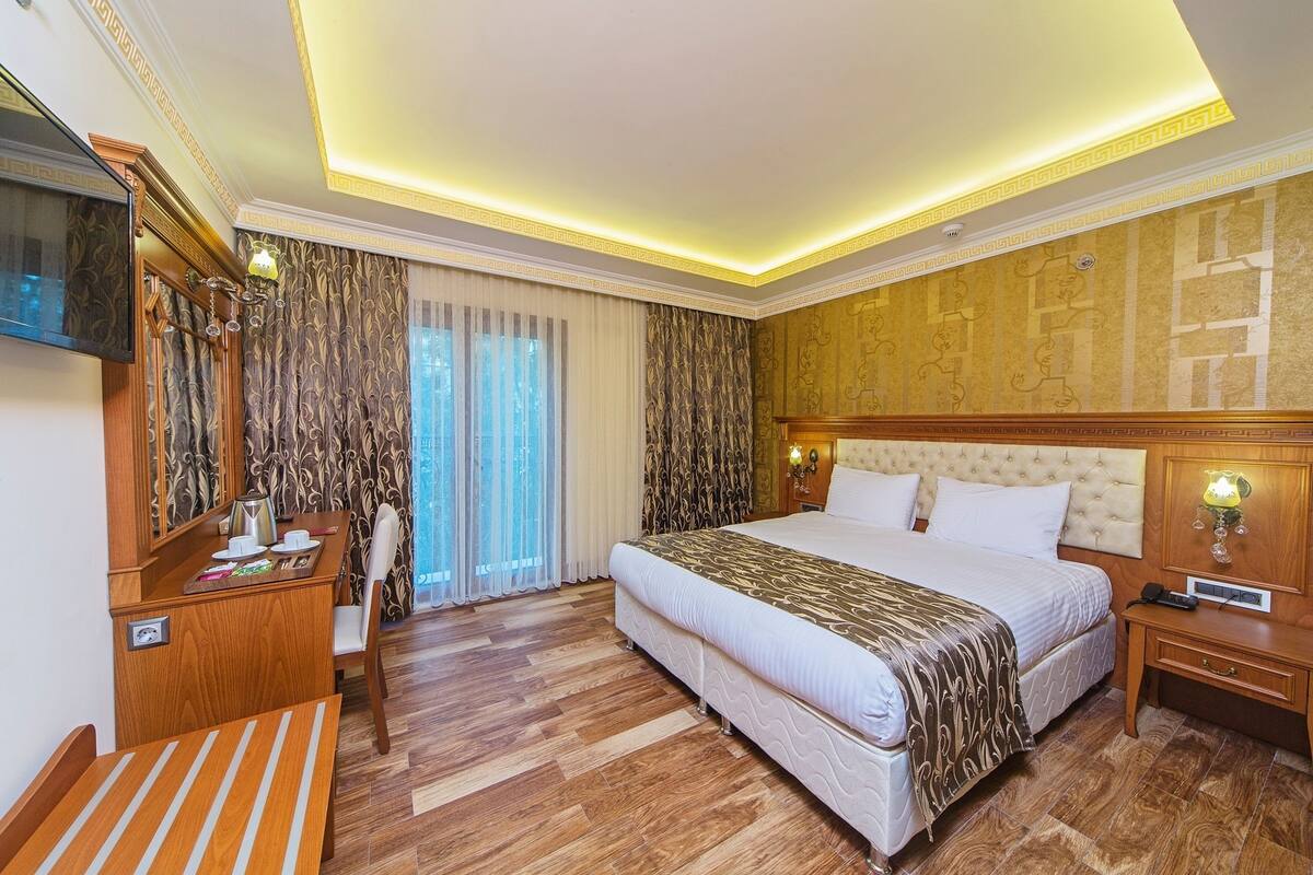 A hotel room with a large bed, a desk with a chair, a TV, and a window with curtains.
