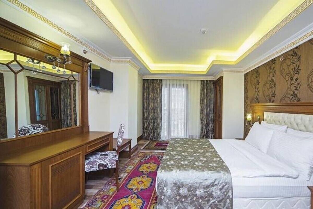 A hotel room with a large bed, a wooden dresser, a TV, and a decorative headboard.