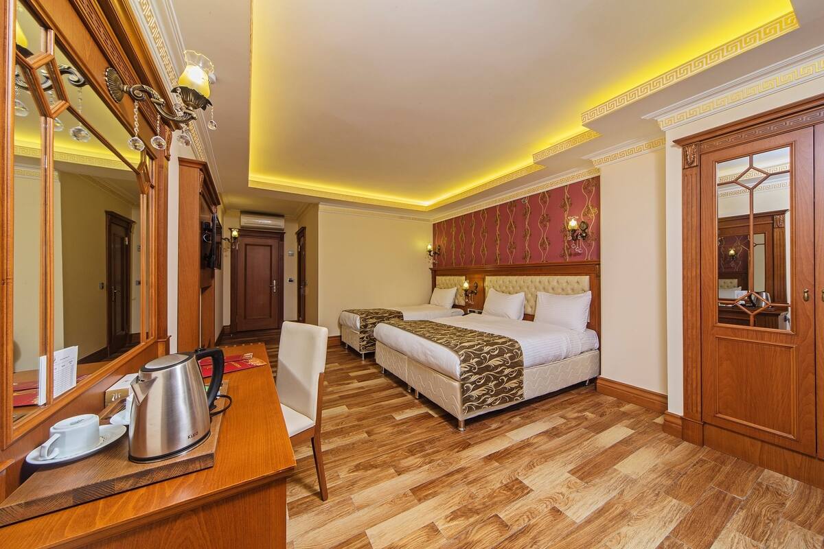 A hotel room with a large bed, two bedside tables, a wooden desk with a kettle, and a mirror.