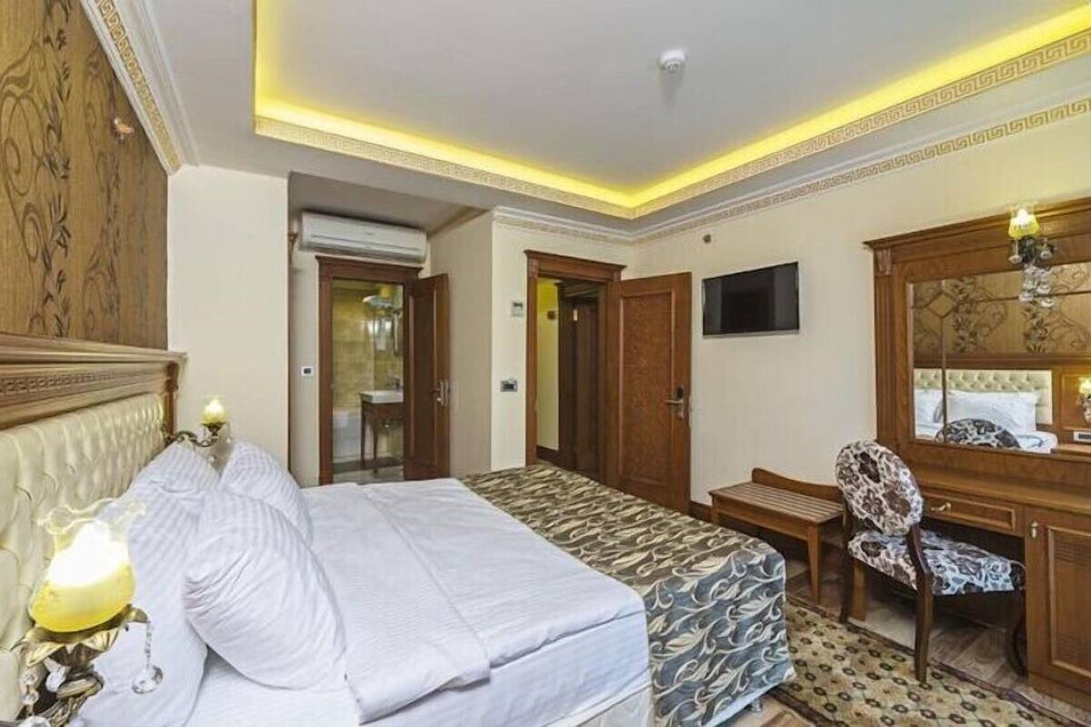 A hotel room with a bed, a desk, a chair, a television, and a mirror.