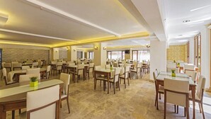 Un comedor amplio con varias mesas y sillas, paredes de piedra y un diseño de techo moderno.