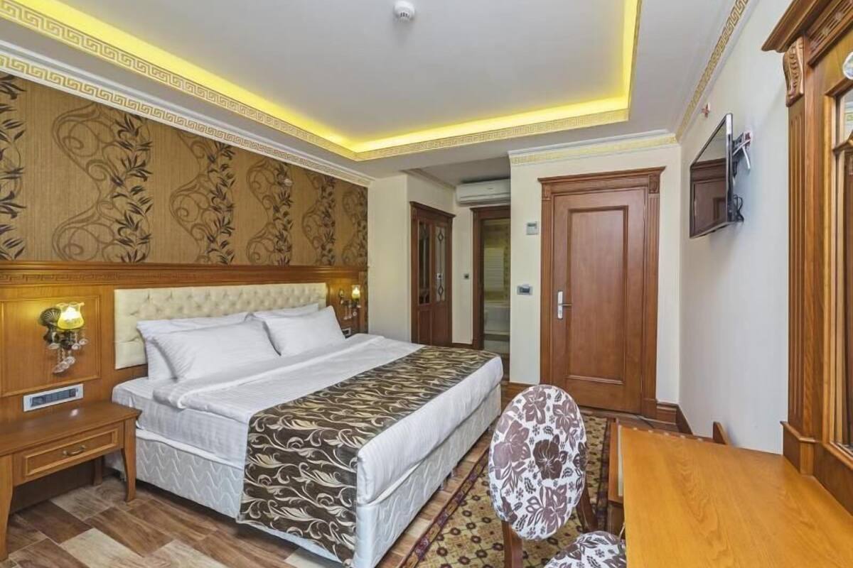 A hotel room with a bed, bedside table, chair, and a TV mounted on the wall.