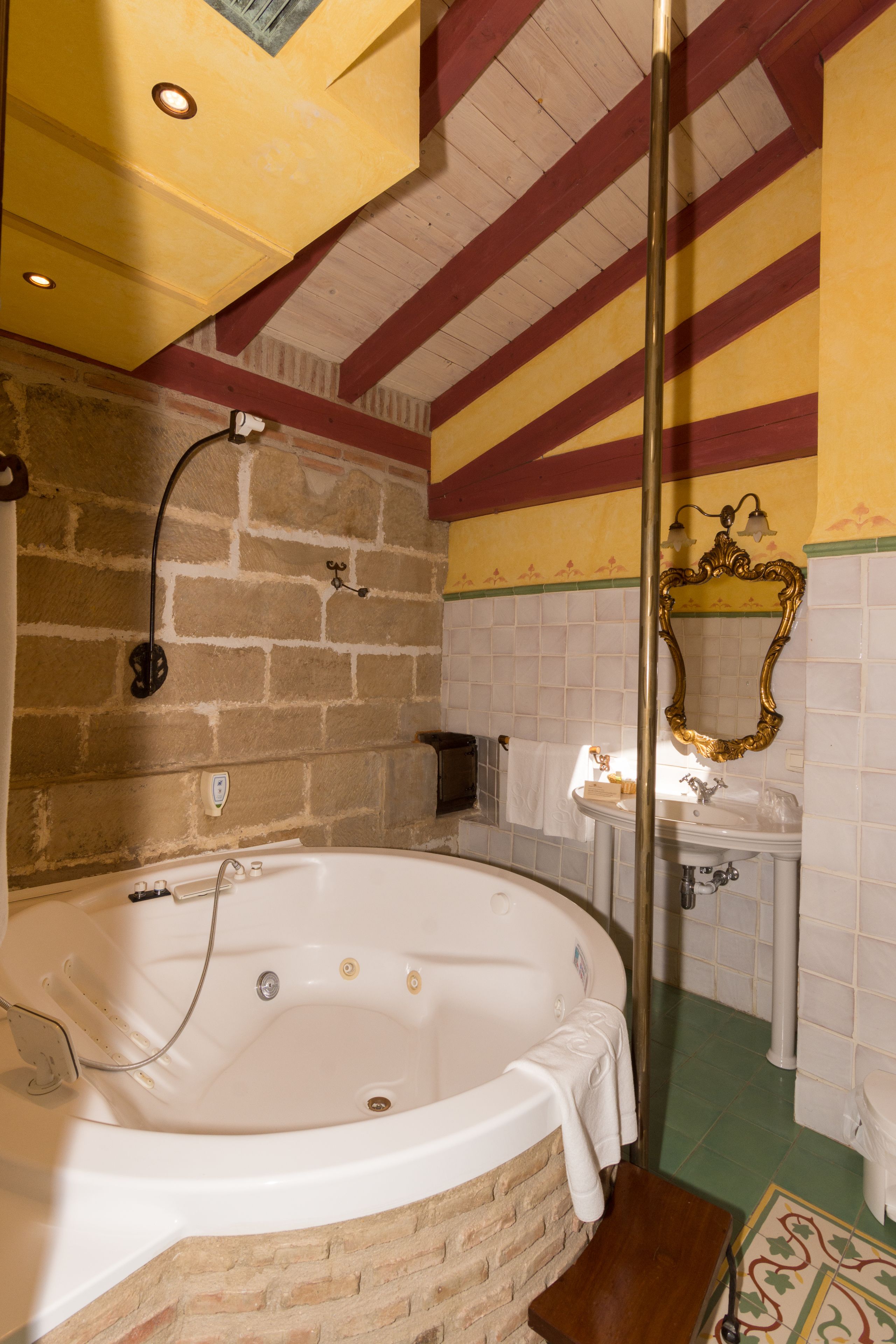 A bathroom with a large bathtub, a wooden bench, a mirror, and a tiled wall.