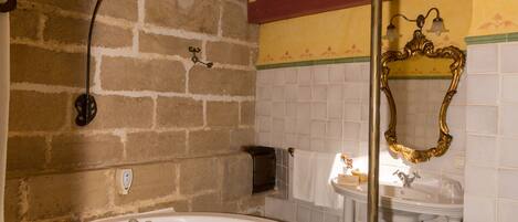 A bathroom with a large bathtub, a wooden bench, a mirror, and a tiled wall.