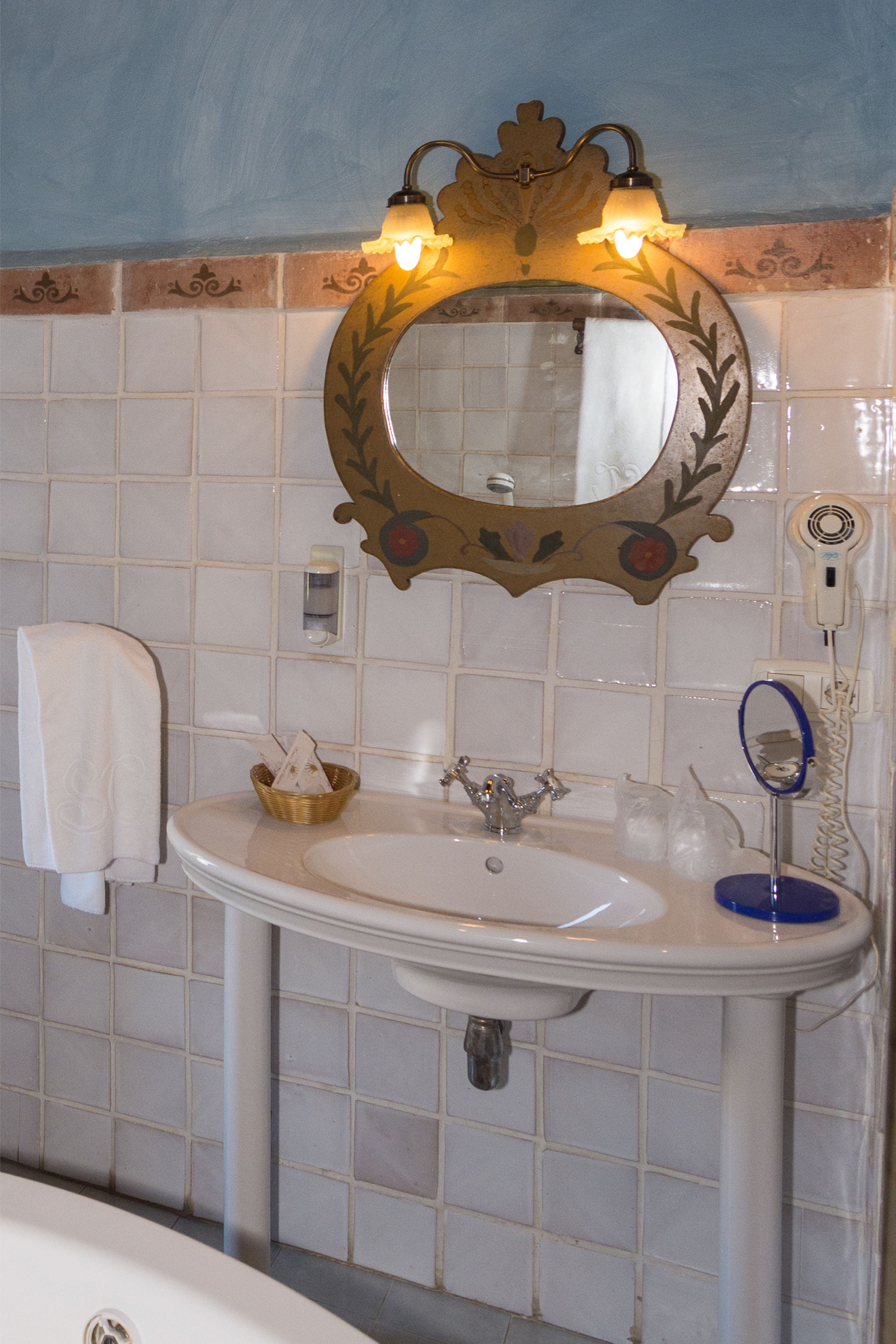 A bathroom with a white sink, a mirror with a decorative frame, a towel hanging on the wall, and a hairdryer plugged in.