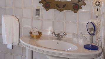 A bathroom with a white sink, a mirror with a decorative frame, a towel hanging on the wall, and a hairdryer plugged in.