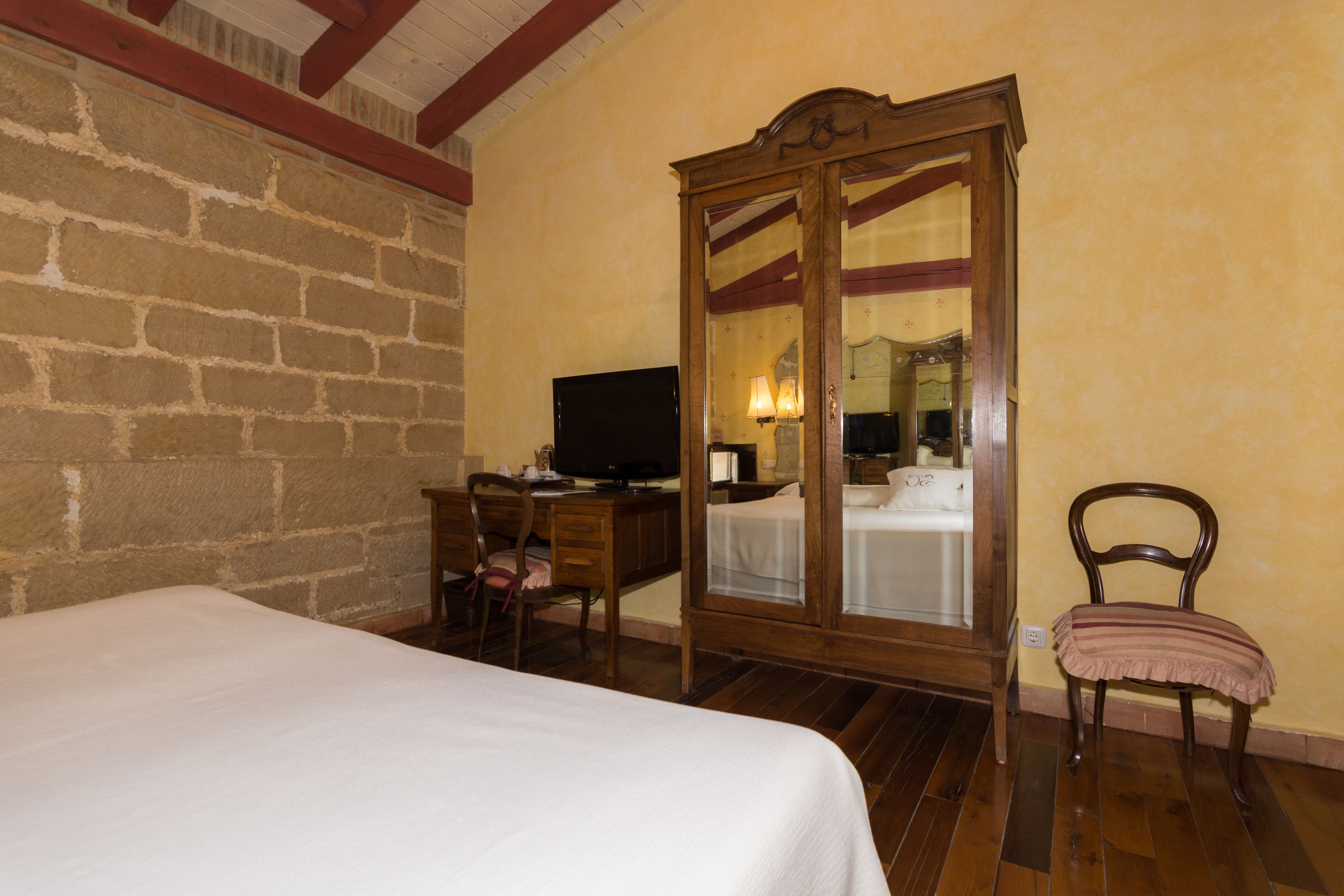 A hotel room with a bed, a desk with a computer, a chair, and a wardrobe.
