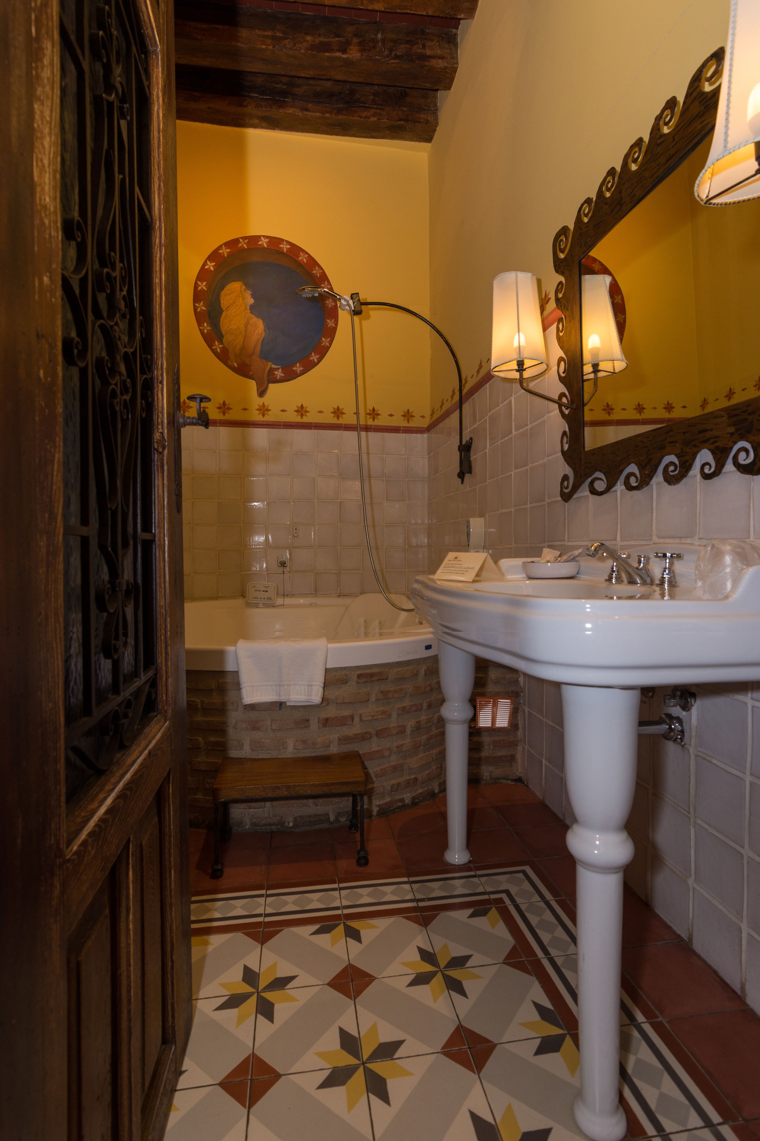 A bathroom with a white sink, a mirror, a bathtub, and a decorative tile floor.