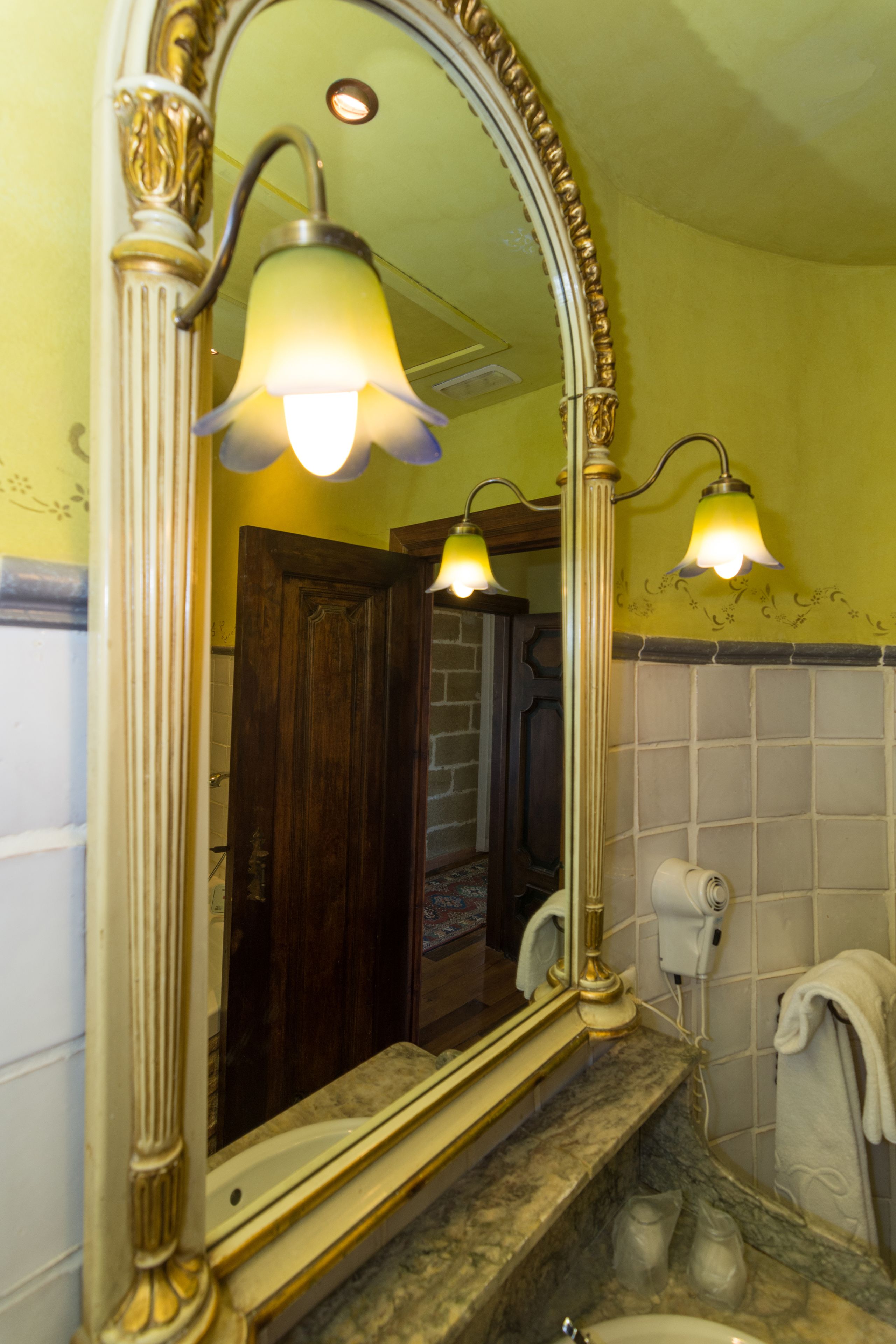 Een badkamer met een grote spiegel, twee wandlampen, een handdoekhouder en een haardroger.