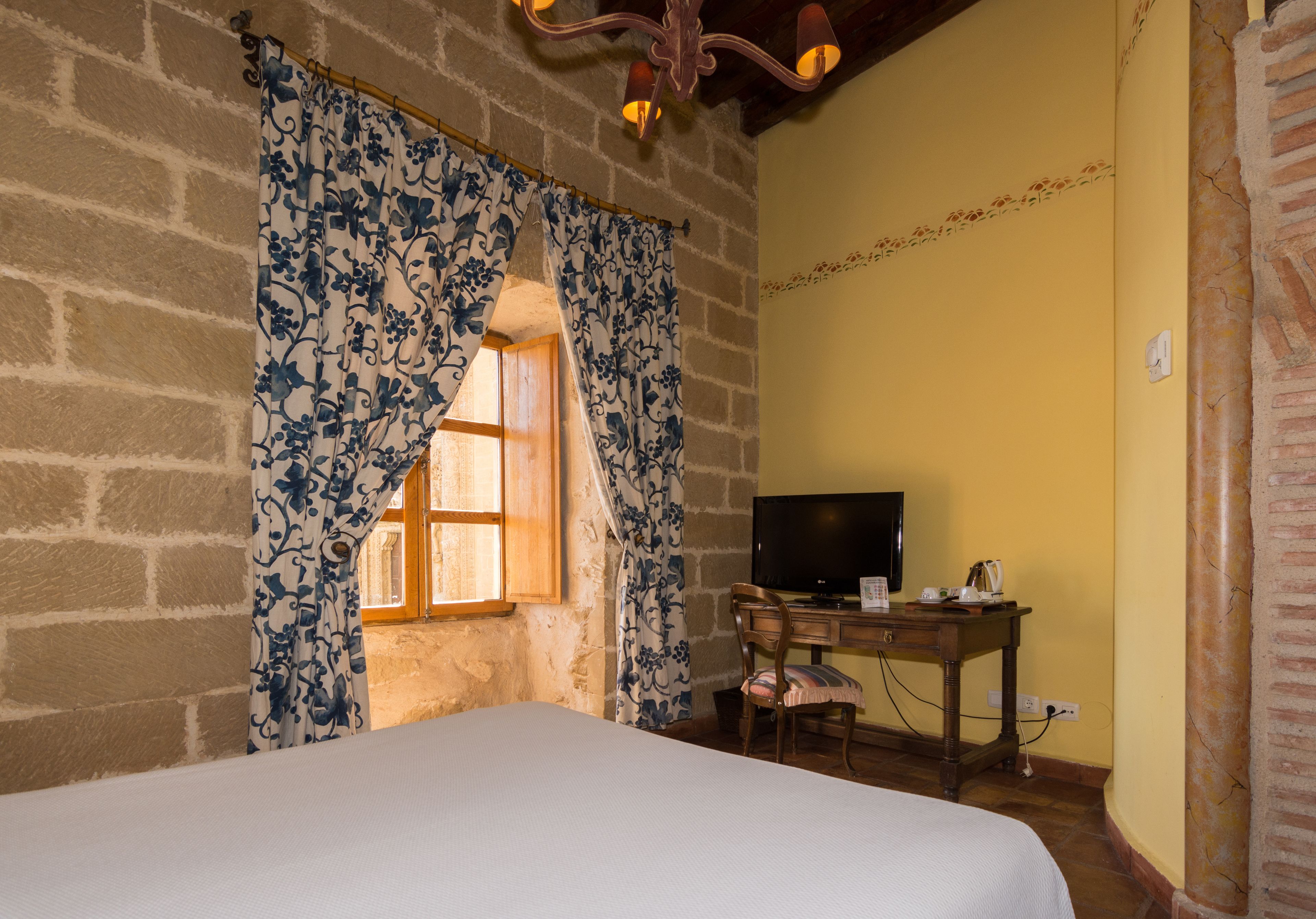 Una habitación con cama, escritorio con televisor y ventana con cortinas.